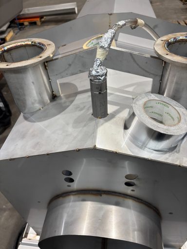Detail van een metalen apparaat met meerdere aansluitingen en een leidingsysteem.