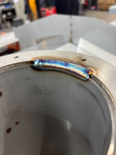 Close-up van een gekleurde lasnaad op een metalen cilindrische structuur.