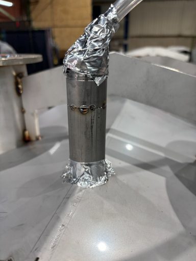 Detail van een metalen buis met folie in een industriële omgeving.